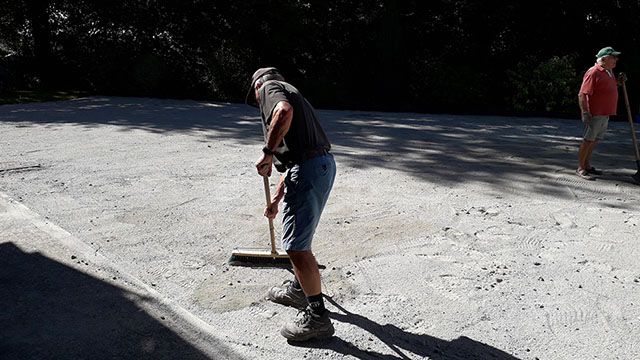 retraité qui tamise le sol pour avoir un terrain de pétanque droit